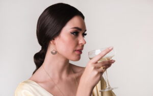 Femeie cu cercei candelabru si pahar cu gin in mana