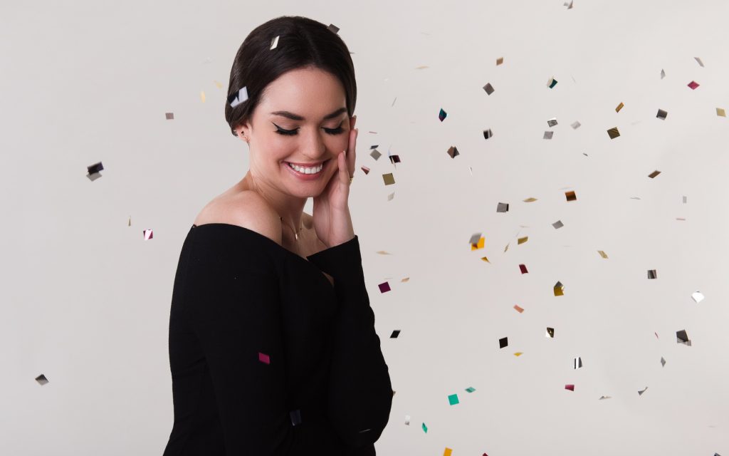 Tânără în bluză neagră care zâmbește, cu cercei în urechi și confetti