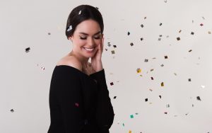 Tânără în bluză neagră care zâmbește, cu cercei în urechi și confetti